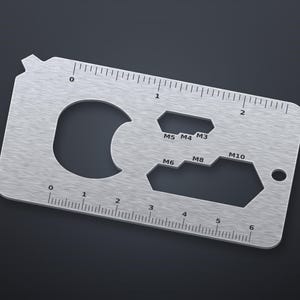 May include: A rectangular silver-colored metal multi-tool card featuring a ruler along the top edge marked in inches and a ruler along the bottom edge marked in centimeters up to 6 cm. It includes a bottle opener, a circular hole, and wrench cutouts labeled M3, M4, M5, M6, M8, and M10.