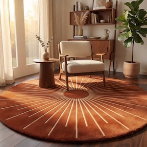 May include: A large, circular, rust-colored area rug featuring a central solid circle with radiating lines extending outward toward the edge. The rug has a soft, plush texture and is positioned on a dark wood floor beneath a wooden chair.