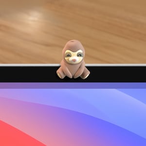 May include: A brown sloth webcam cover with a smiling face, sitting on a laptop screen.