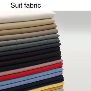 Puede incluir: Una pila vertical de telas para traje dobladas en varios colores, incluyendo blanco, beige, arena, gris, carbón, negro, rosa, rojo, azul claro, azul marino y amarillo. El texto 'Suit fabric' está impreso en negro en la parte superior.