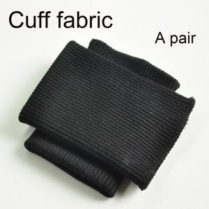 May include: A pair of black ribbed cuff fabric pieces. The image includes the text Cuff fabric and A pair. These rectangular fabric components feature a consistent vertical ribbed texture throughout, designed for garment finishing and construction.