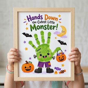 Op de afbeelding: Een ingelijste print met de tekst Hands Down the Cutest Little Monster! en een groene handafdruk die is vormgegeven als een Frankenstein-monster. Het ontwerp bevat een pompoen, een maansikkel, vleermuizen, sterren en illustraties van snoepjes.