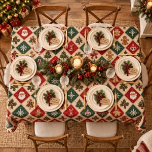 Peut inclure: Une nappe rectangulaire à motif losange rouge, vert et crème, ornée d'illustrations de Père Noël, de bonshommes en pain d'épices, de sapins et de flocons. Quatre assiettes blanches sont décorées de branches de sapin et d'étiquettes.