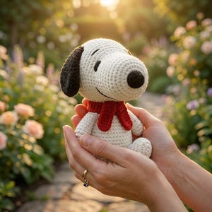 May include: A small, off-white crocheted beagle figurine featuring a black ear, a black nose, and a bright red scarf wrapped around its neck. The character has embroidered black eyes and a simple stitched smile on its rounded head.