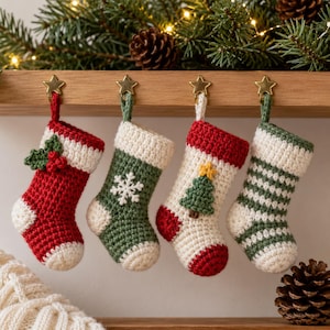 Könnte beinhalten: Vier kleine gehäkelte Weihnachtsstrümpfe hängen an einem Holzregal. Der erste ist rot mit weißem Bündchen und Stechpalmen-Applikation. Der zweite ist grün mit einer weißen Schneeflocke. Der dritte ist weiß mit einem grünen Baum. Der vierte ist grün-weiß gestreift.