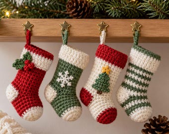 Könnte beinhalten: Vier kleine gehäkelte Weihnachtsstrümpfe hängen an einem Holzregal. Der erste ist rot mit weißem Bündchen und Stechpalmen-Applikation. Der zweite ist grün mit einer weißen Schneeflocke. Der dritte ist weiß mit einem grünen Baum. Der vierte ist grün-weiß gestreift.