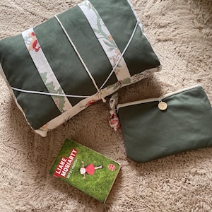 Peut inclure: Une housse de livre rectangulaire en tissu vert olive avec des bandes à motifs floraux blancs et une fermeture élastique blanche, une pochette zippée assortie vert olive avec un bouton en bois et le livre Liane Moriarty Set et Match.