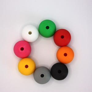 Op de afbeelding: Een verzameling van acht ronde, gladde kralen gerangschikt in een cirkelvormig patroon. De kralen zijn wit, groen, rood, oranje, zwart, grijs, geel en roze van kleur. Elke kraal heeft een enkel, gecentreerd rond gat om te rijgen.