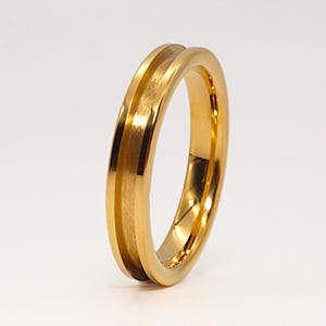 May include: A gold-coloured ring featuring a polished, reflective outer edge and a recessed, brushed-finish centre channel. The band has a smooth, rounded profile with a consistent metallic lustre throughout its circular structure.