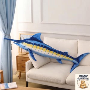 Puede incluir: Un peluche grande de pez marlín azul y amarillo con un pico largo y puntiagudo, una aleta dorsal prominente y una cola bifurcada. El peluche presenta un degradado de azul en la parte superior y una parte inferior amarilla con rayas.