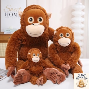 Puede incluir: Tres peluches de orangután de color marrón en diferentes tamaños, cada uno con pelaje desgreñado, cara de color beige claro, ojos grandes y redondos y orejas pequeñas. Los peluches están dispuestos con el más grande detrás y dos más pequeños delante.