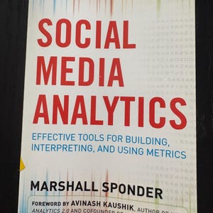 May include: A book titled Social Media Analytics: Effective Tools for Building, Interpreting, and Using Metrics by Marshall Sponder. The cover features red text, a quote by Philip Sheldrake, and a foreword by Avinash Kaushik on a white background.