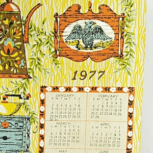 May include: A vintage 1977 kitchen towel with a yellow background and a woodgrain pattern. The towel features a calendar with illustrations of kitchen items like a coffee pot, a butter churn, a pitcher, and a pot. The calendar includes the months of January through December.