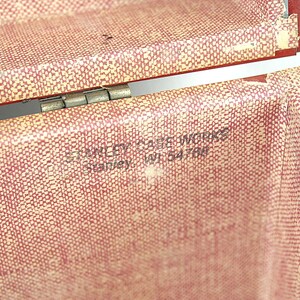 May include: Close-up of an open vintage red and cream-colored case. The case has a textured pattern and a metal hinge. The text "STANLEY CASE WORKS Stanley, WI 54766" is printed on the inside of the case.