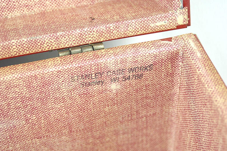 May include: Close-up of an open vintage red and cream-colored case. The case has a textured pattern and a metal hinge. The text "STANLEY CASE WORKS Stanley, WI 54766" is printed on the inside of the case.