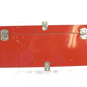 May include: A rectangular red trunk with silver metal hardware. The trunk has a white top edge and silver corner protectors. The trunk has two silver latches and a single latch on the bottom. The trunk is likely vintage.