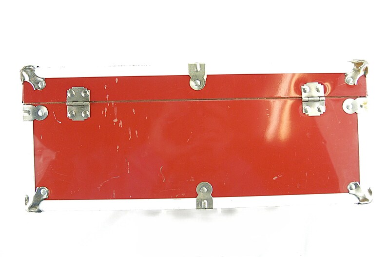 May include: A rectangular red trunk with silver metal hardware. The trunk has a white top edge and silver corner protectors. The trunk has two silver latches and a single latch on the bottom. The trunk is likely vintage.