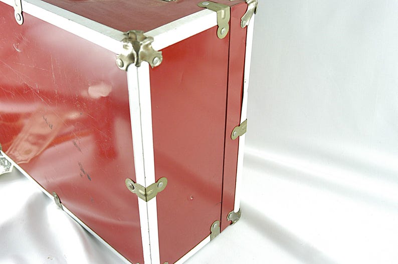 May include: A vintage red trunk with white trim and metal corner protectors. The trunk has a rectangular shape and is made of a sturdy material. The metal hardware is a gold color. The trunk is likely used for storage or travel.