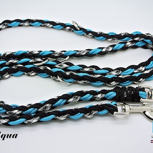 Pode incluir: Uma trela para cães trançada em preto, branco e azul aqua com dois clipes prateados. A trela é etiquetada como "Liz's Leashes" e "Lab Tested, Lab Approved".