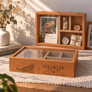 May include: A rectangular wooden keepsake box with a glass lid, featuring an engraved bearded dragon, the name CHARLIE, the years 2018-2026, and the text Forever Our Little Dragon. The box has internal compartments for storing mementos.