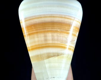 May include: A polished, fan-shaped stone specimen featuring horizontal bands of translucent white, cream, and warm amber-orange colors. The surface is smooth and glossy, displaying natural mineral layers that transition from a wide top to a narrower base.