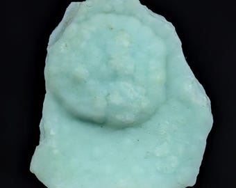 May include: A raw, light mint-green mineral specimen with a botryoidal, rounded cluster formation on its surface. The stone features a matte, opaque texture with subtle variations in color intensity across its irregular, jagged edges.
