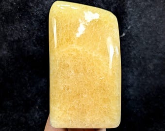 May include: A polished, rectangular-shaped yellow calcite stone with a smooth, glossy surface. The mineral displays a translucent, honey-yellow hue with visible internal crystalline structures and natural veining throughout the piece.