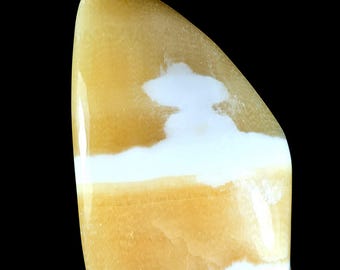 May include: A polished, freeform mineral specimen featuring a smooth, glossy surface with alternating bands of translucent golden-yellow and opaque white. The stone has a curved, asymmetrical shape with a rounded top and a flat base.