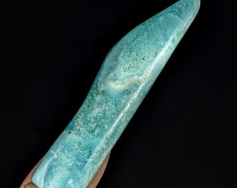 May include: A polished, elongated crystal tower with a smooth, tapered point. The stone features a vibrant teal and turquoise color palette with intricate, marbled white and light green mineral inclusions throughout its textured, crystalline surface.