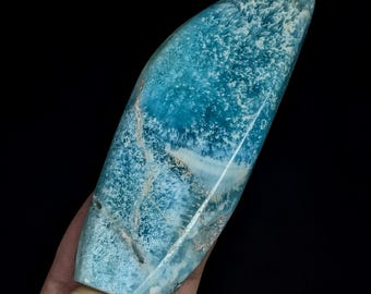 May include: A polished, elongated, teardrop-shaped piece of blue larimar stone featuring intricate white, fern-like crystalline patterns and natural veining throughout the surface, displaying a smooth, glossy texture and vibrant turquoise hues.