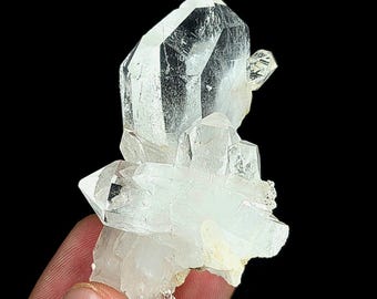 May include: A clear, multi-pointed quartz crystal cluster featuring a large, prominent central point surrounded by several smaller, translucent crystalline formations. The mineral specimen displays natural facets and internal inclusions.