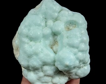 May include: A raw mineral specimen featuring a botryoidal habit with smooth, rounded, bubble-like formations in a pale mint green color. The surface displays a glossy, waxy luster with subtle variations in texture and small, recessed white areas.