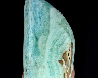 May include: A polished, freeform mineral specimen featuring a vibrant spectrum of turquoise, teal, and sky blue hues. The stone displays intricate, wavy banding patterns and crystalline textures, with a distinct patch of earthy brown mineral inclusion.