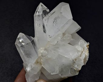 May include: A cluster of clear, translucent quartz crystals with sharp, pointed terminations. The mineral specimen features multiple hexagonal prisms growing together from a common base, displaying natural facets and internal inclusions.