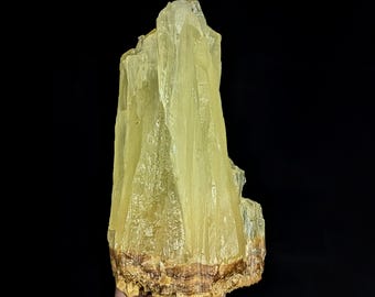 May include: A vertical, translucent pale yellow mineral specimen with a crystalline, fibrous structure. The top section features sharp, elongated points, while the base displays a distinct horizontal band of textured, earthy brown mineral deposits.