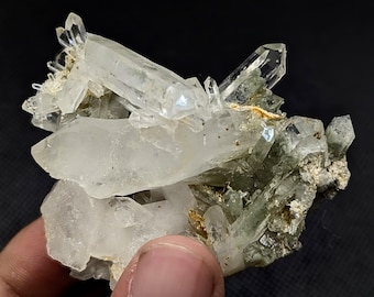 May include: A cluster of clear, translucent quartz crystals with sharp, pointed terminations. The mineral specimen features a mix of large, prismatic crystals and smaller, jagged formations with earthy, greenish-grey mineral inclusions.