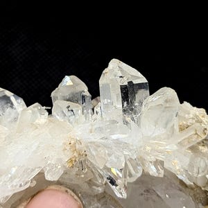 May include: A cluster of clear, pointed quartz crystals with sharp, multifaceted edges and translucent surfaces. The mineral formation features several prominent vertical points rising from a base of smaller, jagged crystalline structures.