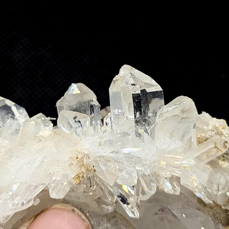 May include: A cluster of clear, pointed quartz crystals with sharp, multifaceted edges and translucent surfaces. The mineral formation features several prominent vertical points rising from a base of smaller, jagged crystalline structures.