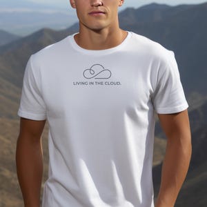 May include: A white short-sleeved t-shirt featuring a minimalist black line drawing of a cloud centered on the chest. Below the cloud graphic, the text reads "LIVING IN THE CLOUD." in a simple, clean, sans-serif black font. The shirt has a crew neckline.