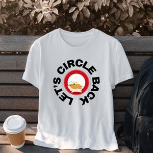 May include: A white short-sleeved t-shirt featuring a graphic of a running hamster inside a red circle. The text "LET'S CIRCLE BACK" is printed in bold black capital letters in a circular arrangement around the central hamster illustration.