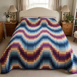 May include: A bed quilt featuring a repeating chevron pattern made of small square fabric patches. The design displays a gradient of colours including deep navy blue, royal blue, light blue, soft lavender, magenta, and warm golden yellow tones.
