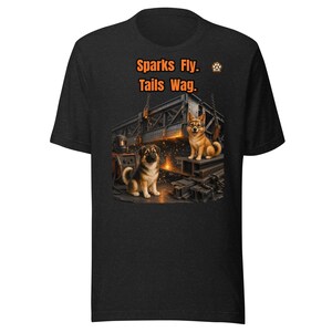 Może przedstawiać: Czarny t-shirt z grafiką przedstawiającą dwa psy w warsztacie metalowym. Jeden pies ma na sobie okulary ochronne i siedzi na stalowych belkach. Nad psami znajduje się pomarańczowy napis "Sparks Fly. Tails Wag." oraz małe logo z odciskiem łapy.