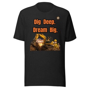 Może przedstawiać: Czarny t-shirt z krótkim rękawem z pomarańczowym napisem Dig Deep. Dream Big. nad grafiką żółtej koparki kopiącej w ziemi, obok której stoi pies w żółtym kasku budowlanym i kamizelce odblaskowej, oraz małym logo z odciskiem łapy.