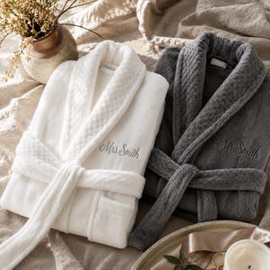 Peut inclure: Un peignoir en peluche blanc avec le texte brodé Mrs. Smith et un peignoir en peluche gris foncé avec le texte brodé Mr. Smith. Les deux peignoirs présentent un col châle à motif gaufré, des manches longues et une ceinture assortie.