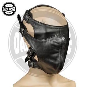 Peut inclure: Un masque facial en cuir noir doté d'une section structurée pour le nez et le menton, fixé par plusieurs sangles réglables et des boucles métalliques argentées. Le masque couvre le bas du visage et les côtés, avec le logo Dark Desire Leathers.