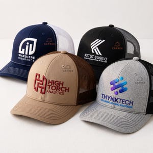 Puede incluir: Cuatro gorras tipo camionero con parte trasera de malla y logotipos bordados. Una azul marino con malla blanca, una negra con malla negra, una beige con malla marrón y una gris jaspeado con malla negra. Cada una tiene logos y texto.
