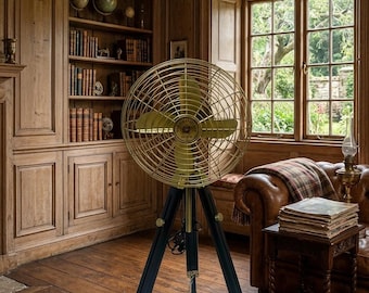 May include: A vintage-style floor fan featuring a circular brass-toned metal cage and blades mounted on a dark wooden tripod stand with adjustable legs and metallic accents. The center of the fan includes a small circular emblem with text.