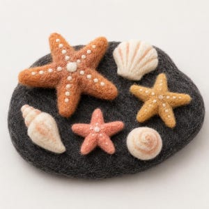 May include: A dark gray felted wool base shaped like a stone, adorned with three needle-felted starfish in orange, yellow, and pink, along with three off-white felted seashells of varying shapes, all featuring textured surfaces and small details.
