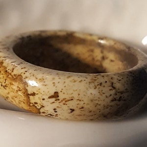 May include: A smooth, light brown ring with a speckled pattern. The ring is made of natural stone and has a polished finish.