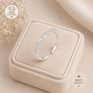 May include: A silver-toned open ring featuring a twisted band design with small clear stones embedded along the top half. The metal band has a smooth finish and includes a visible S925 hallmark stamp on the inner surface of the ring.
